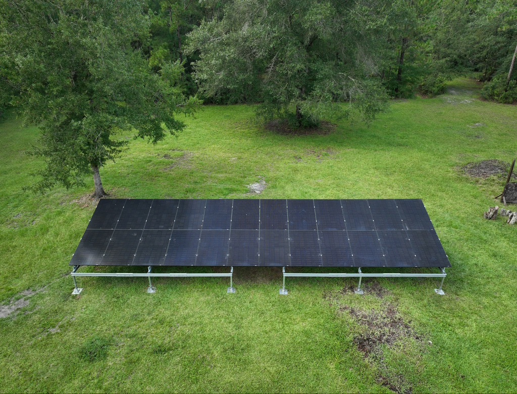 Ground-mount solar array on a grassy rural property surrounded by trees