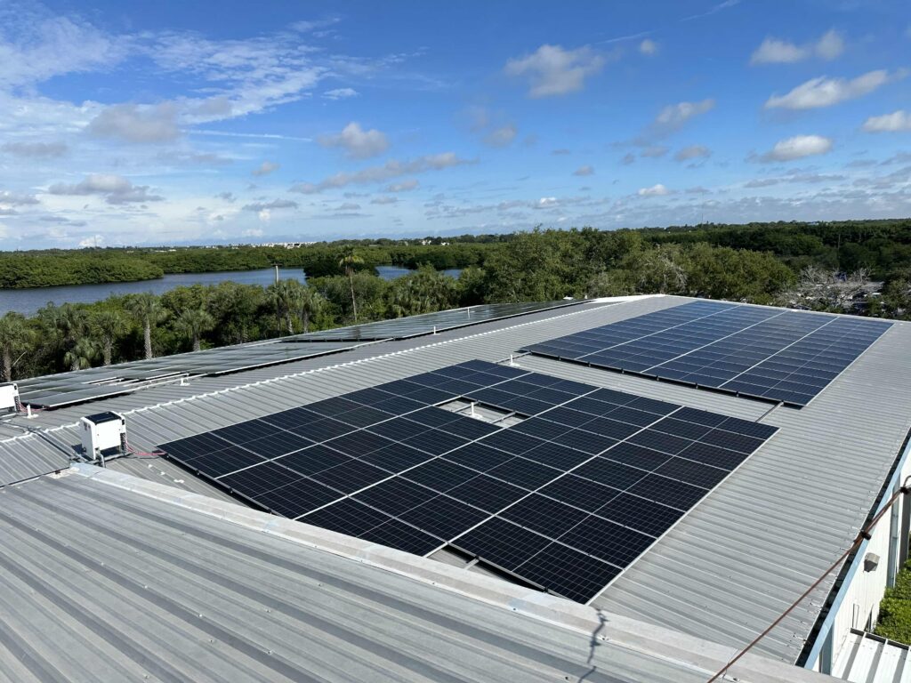Rooftop solar array on a metal commercial roof with a river and trees in the background